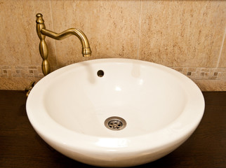 Ceramic sink inside bathroom. Rounded white ceramic sink with golden accessories inside bathroom. 