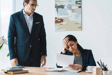 Businessman looking at stressed businesswoman with papers in hands