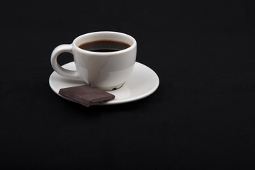 Cup of coffee with chocolate on black surface..