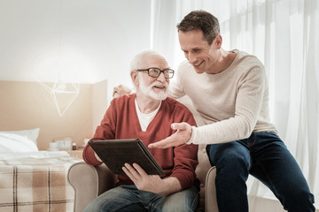 Do you remember. Funny pleasant satisfied men sitting on the chair spending time together and overlooking the tablet.