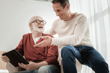 Remember this. Senior unshaken bespectacled man spending time with a son smiling and holding the tablet.