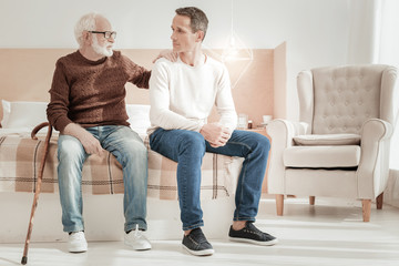 Talk with me. Serious attentive lovely father sitting on the sofa touching to son communicating with his.