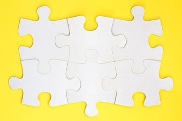 Group of six white paper jigsaw puzzles. Connected blank puzzle pieces on a yellow background....