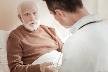 Doctors advices. Attentive pleasant unshaken man being ill in the bed listening to a doctor looking...