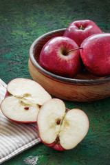 Still life with apples with whole apples in a wooden plate and cut on a dark green background