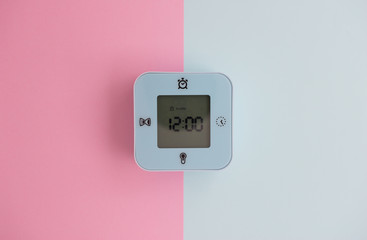 Minimal flat lay concept of blue mini digital alarm clock with LED screen on the colorful pastel background - top view