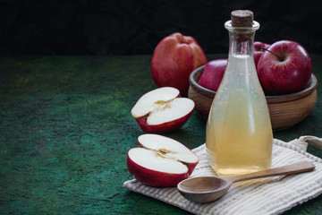 Glass bottle with apple cider vinegar, whole fresh red apples on a green black background