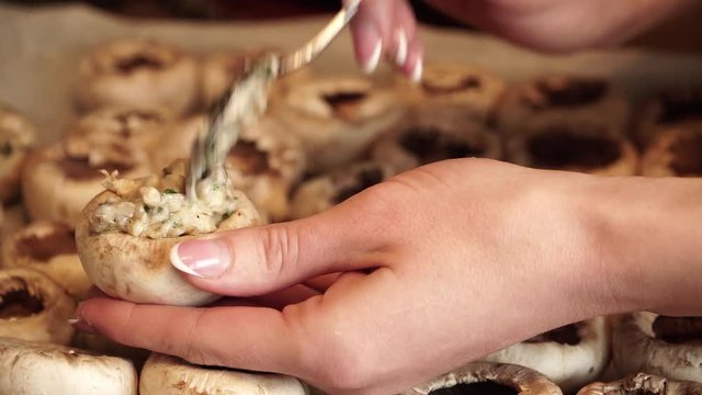 Woman puts stuffing in mushroom caps for cooking delicacy