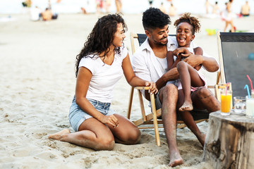 Young mixed race family sitting and relaxing at the beach on beautiful summer day.Parents making fun with they daughter.