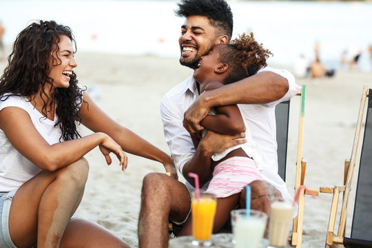 Young mixed race family sitting and relaxing at the beach on beautiful summer day.Parents making fun with they daughter.