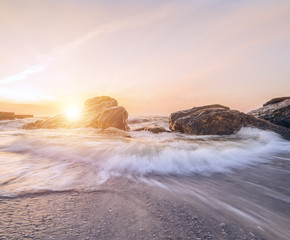 A beautiful dawn on the beach. The wave is approaching the shore. Waves breaking against stones. Long exposure
