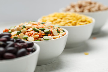 Different beans in bowls on a white wooden table