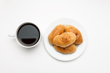 Fresh croissant in a white plate and cup of coffee, top view
