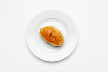 Fresh croissant in a white plate on a white table, top view