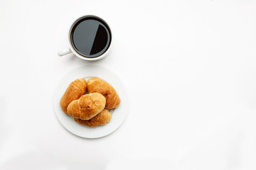 Fresh croissant in a white plate and cup of coffee, top view, text space