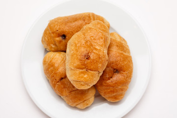 Fresh croissant in a white plate on a white table, top view