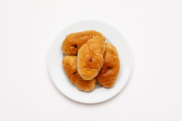 Fresh croissant in a white plate on a white table, top view