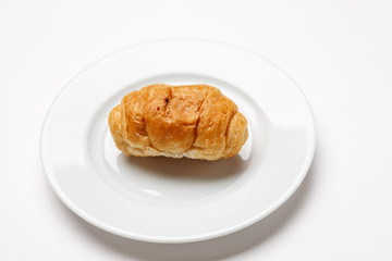 Single fresh croissant in a white plate on a white table