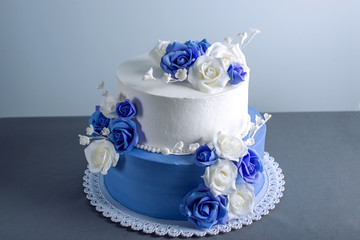 Beautiful two tiered white and blue wedding cake decorated with flowers sugar roses. Concept of elegant holiday desserts