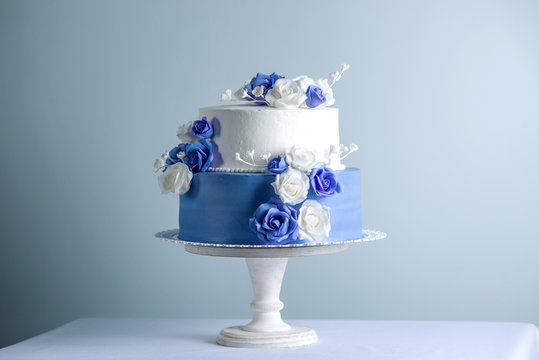 Beautiful two tiered white and blue wedding cake decorated with flowers sugar roses. Concept of elegant holiday desserts