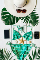 Bikini suit, hat, sunglasses, smartphone, sea star, green plam leaves arranged on wooden baclground. Summer holidays vacation concept. Vertical tropical poster banner, postcard.
