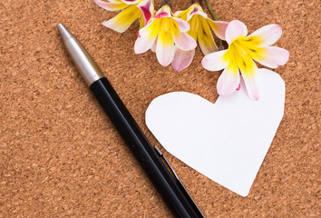 Blank note in shape of heart with copy-spce and flowers, on cork surface.