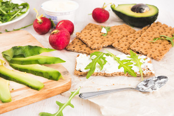 Process of making sandwiches whith green avocado. Red garden radish, arugula, cream cheese, eggs and rye bread crusts. Healthy food on wooden chopping board. 