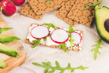 Process of making sandwiches whith green avocado. Red garden radish, arugula, cream cheese, eggs and rye bread crusts. Healthy food on wooden chopping board. 