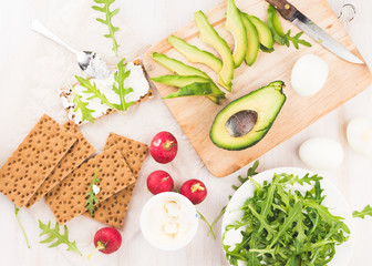 Process of making sandwiches whith green avocado. Red garden radish, arugula, cream cheese, eggs and rye bread crusts. Healthy food on wooden chopping board. 