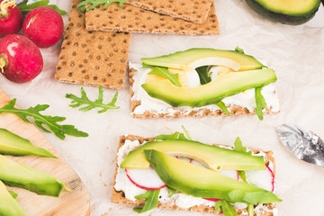 Process of making sandwiches whith green avocado. Red garden radish, arugula, cream cheese, eggs and rye bread crusts. Healthy food on wooden chopping board. 