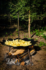 Potatoes fried in oil over a wood fire, cooked outside on unusual round curved metal steel disk with legs and handle. Romanian spring summer and autumn grill and barbecue tradition of cooking for frie