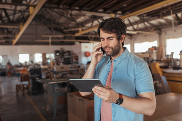Woodworker using a phone and tablet in his large workshop