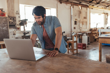 Creative young woodworker creating new designs using a laptop