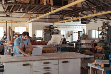 Young woodworker working online at a bench in his workshop