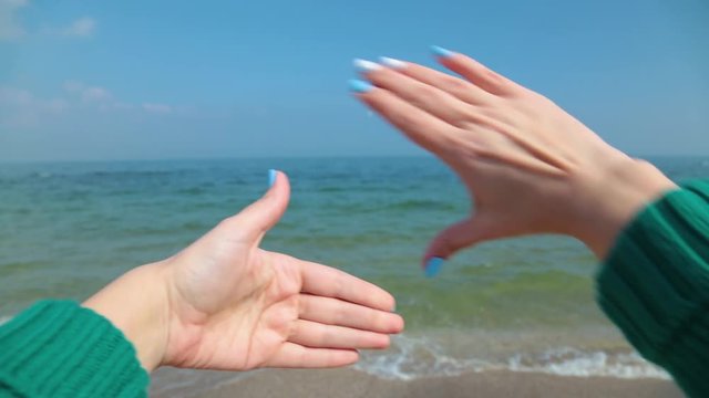 Close up of female caucasian hands isolated on blue sea and sky background. Young woman forms frame with her two hands as if looking at something virtual and invisible in distance. Point of view shot.