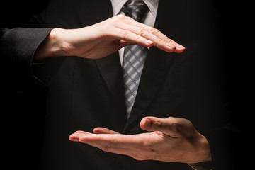 Close up of man in black suit with hand gesture on black background.