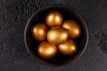 Golden eggs in a black cup on a black textured background. Easter eggs. Top wiev.