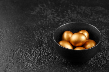 Golden eggs in a black cup on a black textured background. Easter eggs. Eggs, painted in gold for the holiday.
