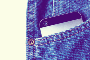 Golden bitcoins and large stack of money with modern smartphone in the pocket of old vintage indigo stonewashed jeans. Concept of daily things of modern man. Ultraviolet style. Close up