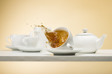 falling cup of tea on white table with tea splashing