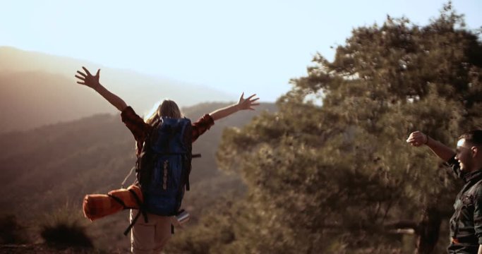Cheerful hikers with arms outstretched reaching mountain peak