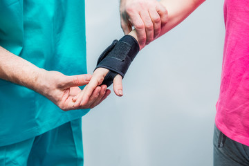 Close up Neurologist doctor, therapist puts on wrist retainer on young female patient's hand. Pain...