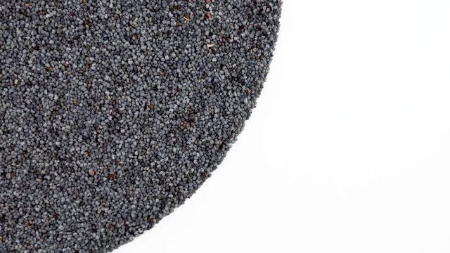 Half frame circle shaped heap of organic raw poppy seeds rotating on turn table. Isolated on white. Loopable. Close up macro. View from above/overhead. 