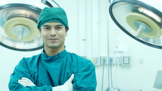 Young man doctor looking to camera with attractive smile at operating room background. Medical concept. 