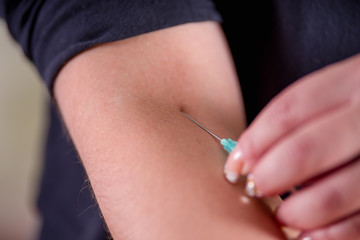 Close up of young woman using herself hands taking a blood sample with a syringe