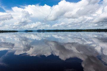 Beautiful reflection of blue sky and clouds in the waters of the Negro River with rainforest and hills in the background.
