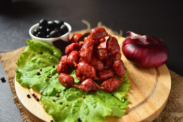 Hunting sausages on a wooden board with lettuce, basil, cherry tomatoes, paprika and olives.