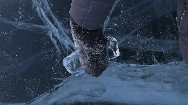 Men in the mittens twists the ice on the ice. Slow motion. The camera moves behind the ice. A piece of icy is very beautifully spinning on ice with magical cracks.