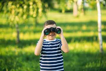 Little boy in a striped t-shirt looks through binoculars .Spring, sunny weather