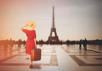 Fototapeta na wymiar Redhead girl with suitcase in Paris with Eiffel tower on background. Concept of travelling around the World
